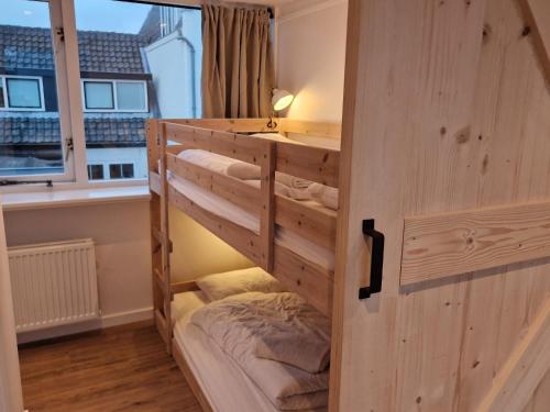 ein Etagenbett aus Holz in einem Zimmer mit Fenster in der Unterkunft Tip! Noordwijk city center house in Noordwijk aan Zee