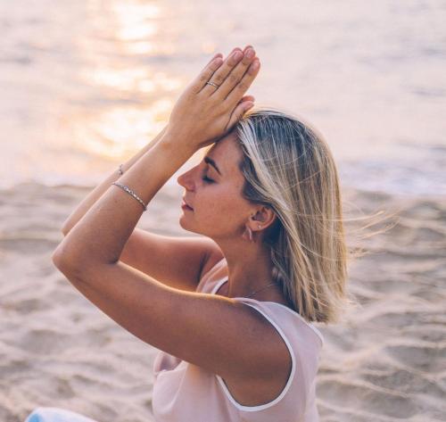 a woman sitting on the beach with her hands on her head at Luxury Beachfront Villa With Private Pool, Private Beach, Yoga & Sea Adventures in Larnaka