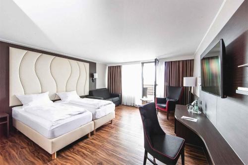 フリードリヒスハーフェンにあるプラザ ホテル フェアー アム ボーデンゼーのベッド、デスク、椅子が備わるホテルルームです。