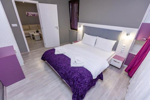 a bedroom with a large bed with a purple blanket at Апартаменти Елеганс in Sandanski