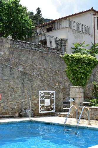 a pool in front of a stone wall and a house at Kyriaki Guesthouse & Suites in Amfiklia