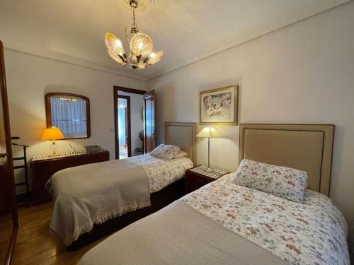 a bedroom with two beds and a chandelier at Elegante apartamento con vistas al puerto de Santander in Santander