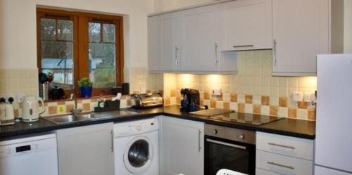 a kitchen with white cabinets and a washing machine in it at Taigh Munro in Aviemore