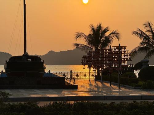 a sunset over the water with palm trees and a boat at Phoenix Flower Hotel in Cat Ba
