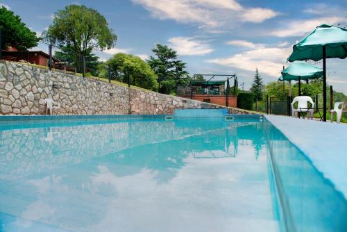 a swimming pool with a stone wall and blue water at Castelar - Hotel & Apart in Huerta Grande