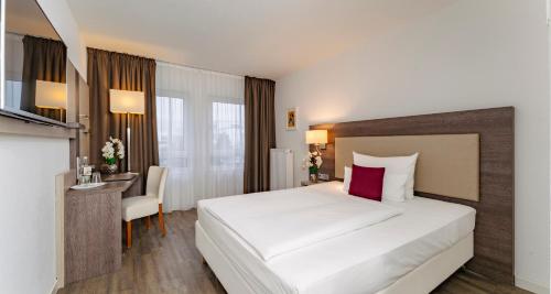 a bedroom with a large white bed and a desk at PLAZA INN Karlsruhe Nord in Karlsruhe