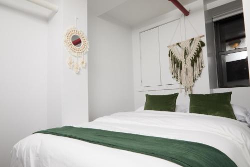 a white bedroom with a white bed with green pillows at Comfy Guest House in Hell's Kitchen in New York