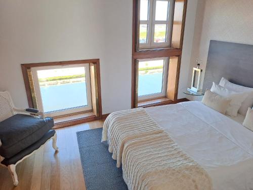a bedroom with a bed and a chair and two windows at SaberAmar City & Ria & More in Aveiro