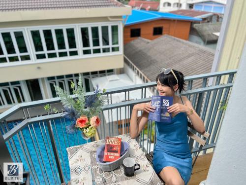 a young woman sitting on a balcony holding a box at Buritel Hotel in Buriram
