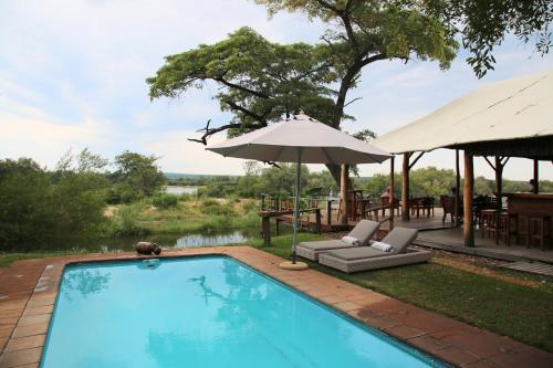 einen Pool mit Sonnenschirm, Stühlen und Tischen in der Unterkunft Zambezi Dusk in Livingstone