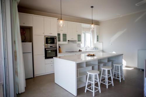 uma cozinha com armários brancos e um balcão com bancos em Villa Aphrodite em Paleros