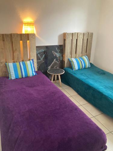 two beds in a room with purple sheets and a table at Sérénité in Biscarrosse