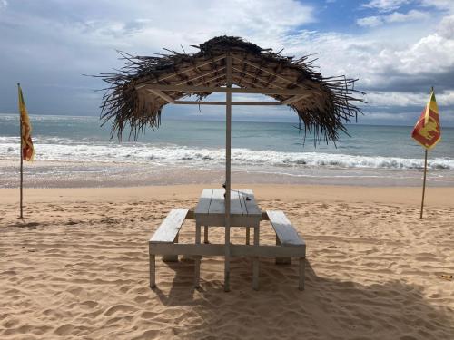 a bench sitting on the beach under an umbrella at Oruwa Turtle Beach Villa in Kosgoda