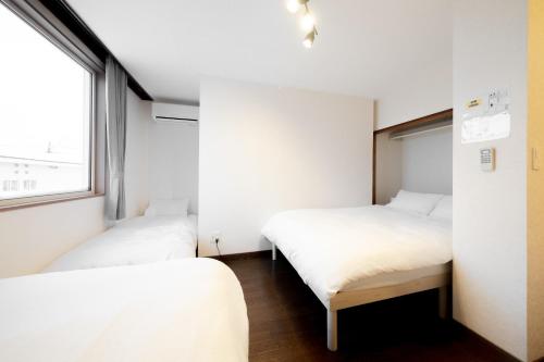 two beds in a small room with a window at Lavender Breeze Furano in Furano
