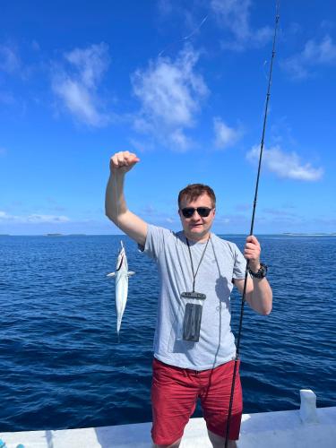 a man standing on a boat holding a fish at Balma Beach Inn in Faafu