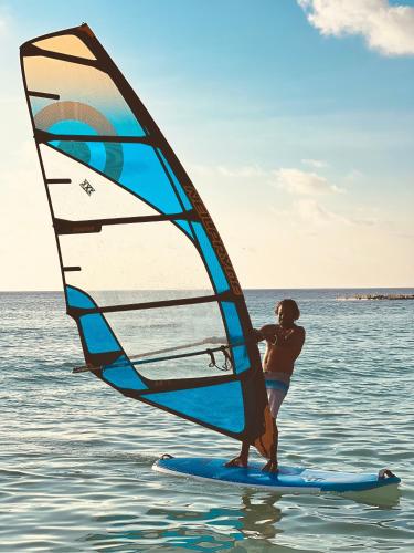 a woman standing on a surfboard with a wind sail at Balma Beach Inn in Faafu