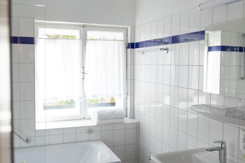 a white tiled bathroom with a sink and a window at Gästehaus Englischer Garten in Munich