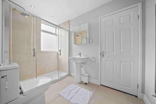 a white bathroom with a toilet and a sink at Queen’s Park, Spacious 3 Bedroom Flat in London