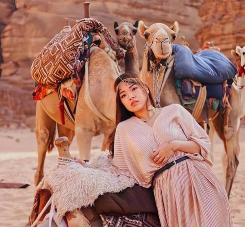 a woman sitting on the ground next to a camel at Nasem rum in Wadi Rum