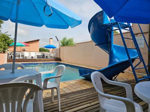a pool with a slide and tables and chairs with blue umbrellas at Pousada Recanto Passarela in Aparecida