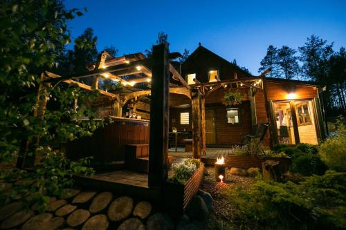 a house with a pergola in the yard at night at Domek całoroczny SÓWKA na Kaszubach z banią i sauną na wyłączność, wspólny basen i bilard z domkiem Jeleniówka - Ostrowite Leśna Dolina in Sulęczyno