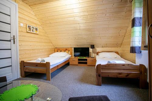 a room with two beds and a tv in a log cabin at Domek całoroczny SÓWKA na Kaszubach z banią i sauną na wyłączność, wspólny basen i bilard z domkiem Jeleniówka - Ostrowite Leśna Dolina in Sulęczyno