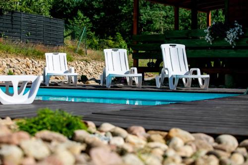 three white chairs sitting next to a swimming pool at Domek całoroczny SÓWKA na Kaszubach z banią i sauną na wyłączność, wspólny basen i bilard z domkiem Jeleniówka - Ostrowite Leśna Dolina in Sulęczyno