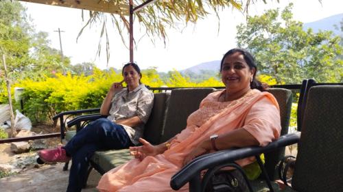 two women sitting on chairs under an umbrella at The Wai Hills MTDC Approved in Wai