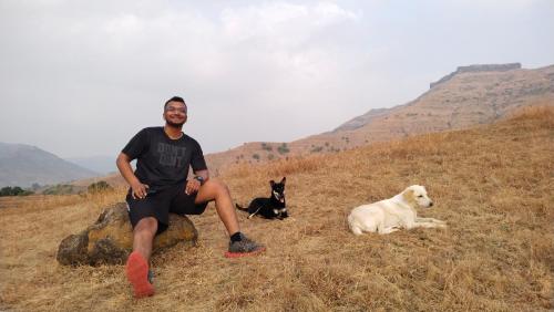 a man is sitting on a hill with two dogs at The Wai Hills MTDC Approved in Wai