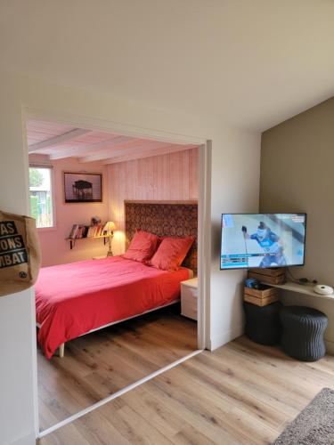 a bedroom with a red bed and a flat screen tv at Chalet 47m2 dans PRL linge fourni in Gujan-Mestras