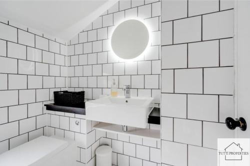 a white tiled bathroom with a sink and a mirror at Elegant Home from Home in Manchester