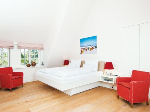 a white bedroom with a white bed and two red chairs at Kuckucksnest in Kampen
