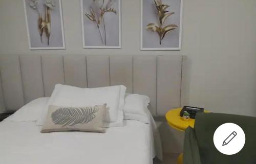 1 dormitorio con cama con almohadas blancas y mesa amarilla en ESPAÇO ACONCHEGANTE NO SUDOESTE, en Brasilia