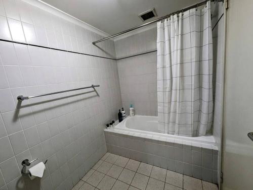 Un baño con bañera y cortina de ducha. en City & lakeside with pool, gym & tennis court, only 15 mins walk into the City, en Perth