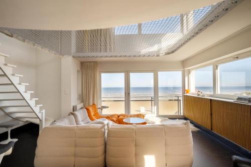 uma sala de estar com um sofá branco e algumas janelas em Vista del Mar Sixties em Koksijde