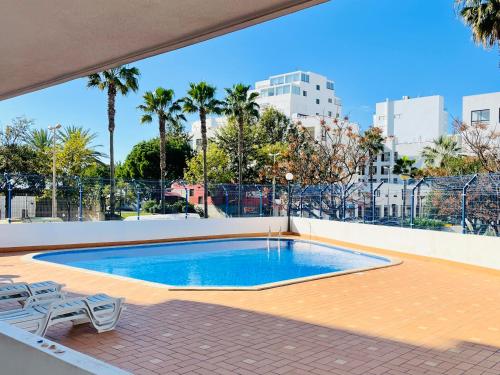 a swimming pool on a patio with chairs and palm trees at Pérola do Algarve in Quarteira