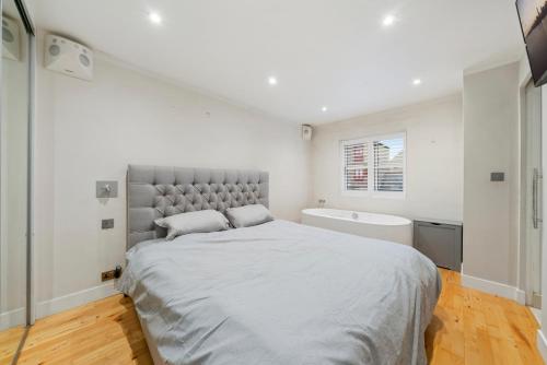 a white bedroom with a bed and a bath tub at Glamorous 2BR House, Outdoor Space & Free Parking in London