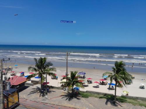 einen Strand mit Palmen und Sonnenschirmen und dem Meer in der Unterkunft Belíssimo apartamento frente mar in Mongaguá