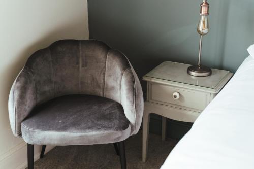 a chair sitting next to a bed next to a nightstand at The Falcon Inn in Painswick