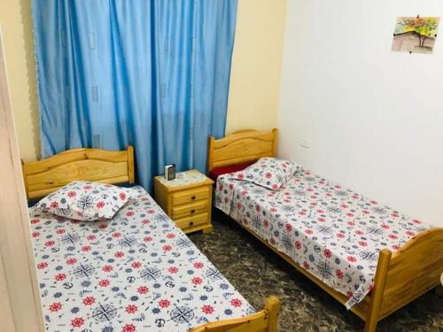 - 2 lits dans une chambre avec des rideaux bleus dans l'établissement Résidence Aquilaria Dar Nouha, à El Haouaria