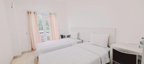 a white bedroom with two white beds and a window at Tos Residence in Tangerang