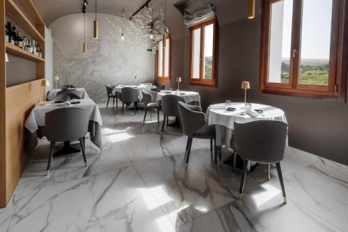 un restaurante con mesas y sillas blancas y ventanas en Boutique Hotel Municipio 1815, en Valdobbiadene