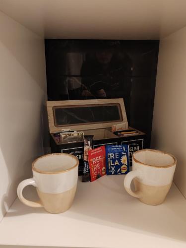 deux tasses à café assises sur une étagère devant une télévision dans l'établissement Hébergement proche aéroport de Nantes, à Saint-Aignan-Grand-Lieu