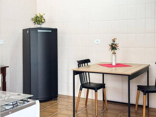 a kitchen with a table and a black refrigerator at Casa Aconchego - O refúgio perfeito para amar e descansar in Peruíbe