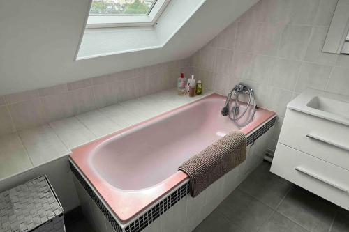 La salle de bains est pourvue d'une baignoire rose et d'une fenêtre. dans l'établissement Duplex Cosy MyFontainebleau Hyper Centre, à Fontainebleau
