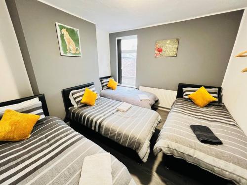 um quarto com três camas com almofadas amarelas em Spacious Retreat: 8BR House in Prime Location em Liverpool