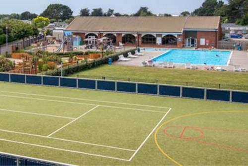 a tennis court with a pool in the background at Lemon Grove in Mudeford