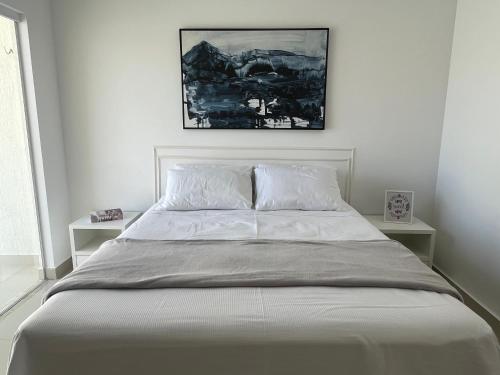 ein Bett mit weißer Bettwäsche und ein Bild darüber in der Unterkunft Casa em PontaNegra Aconchegante in Natal