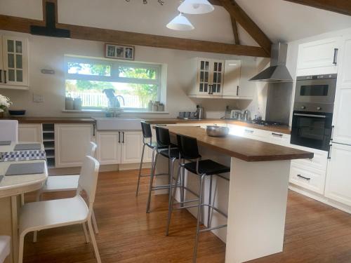 eine Küche mit weißen Schränken und eine Insel mit Barhockern in der Unterkunft Stunning Barn Conversion next to Horse Field sleeps 10 in Morpeth