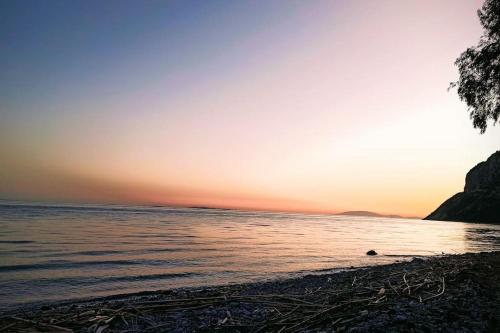 a beach with the sun setting over the water at Rizaki Cottage in Nafpaktos in Nafpaktos